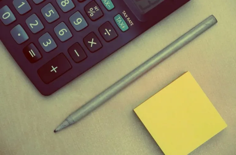 Close-up of calculator keys beside a pencil and a yellow sticky note