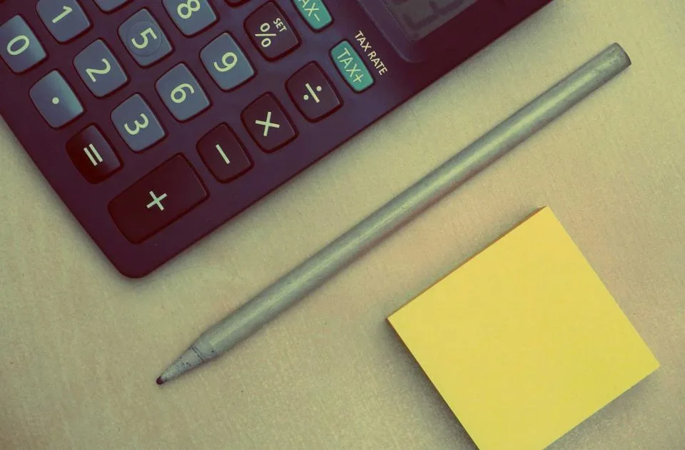 Close-up of calculator keys beside a pencil and a yellow sticky note