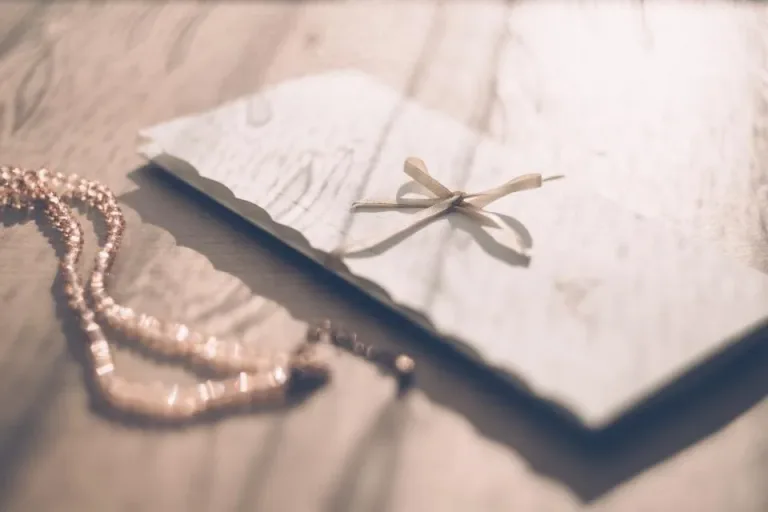 A white envelope tied with a ribbon next to a string of pearls on a table