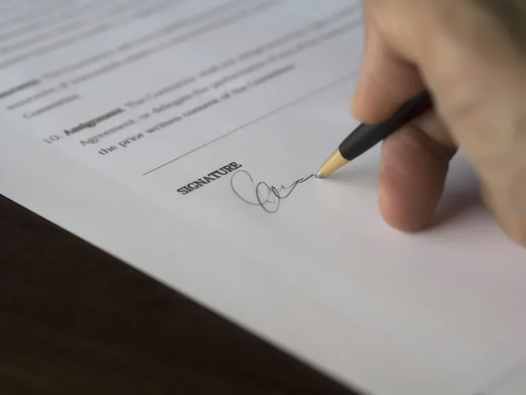 Close-up of a hand signing a printed agreement with a ballpoint pen
