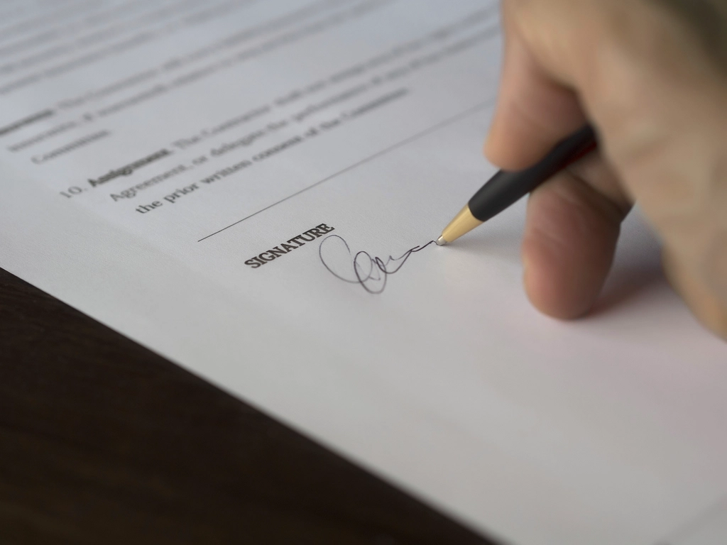 Close-up of a hand signing a printed agreement with a ballpoint pen