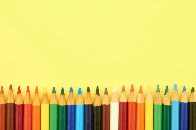 A row of colored pencils lined up against a yellow background