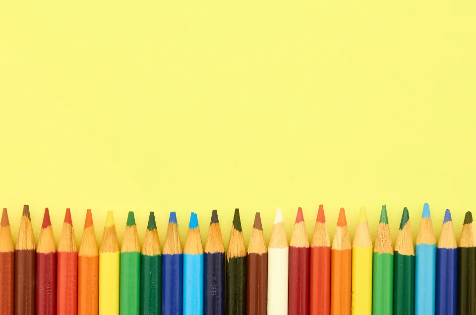 A row of colored pencils lined up against a yellow background