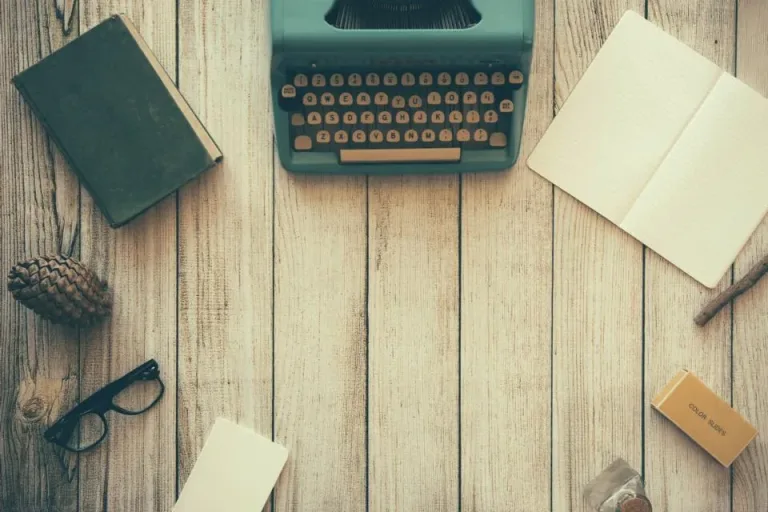 Flat lay of a vintage typewriter, notebooks and glasses on a wooden desk