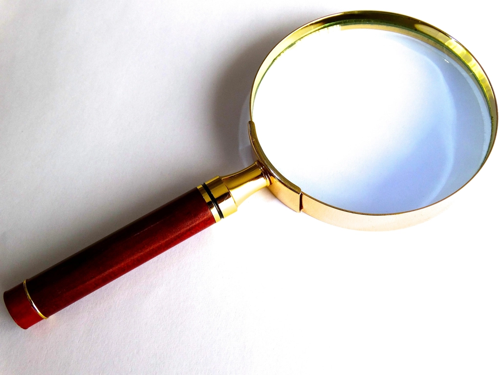 A vintage brass magnifying glass with a red handle on a white background