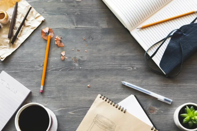 Top view of a writing desk with notebooks, pencils and a cup of coffee